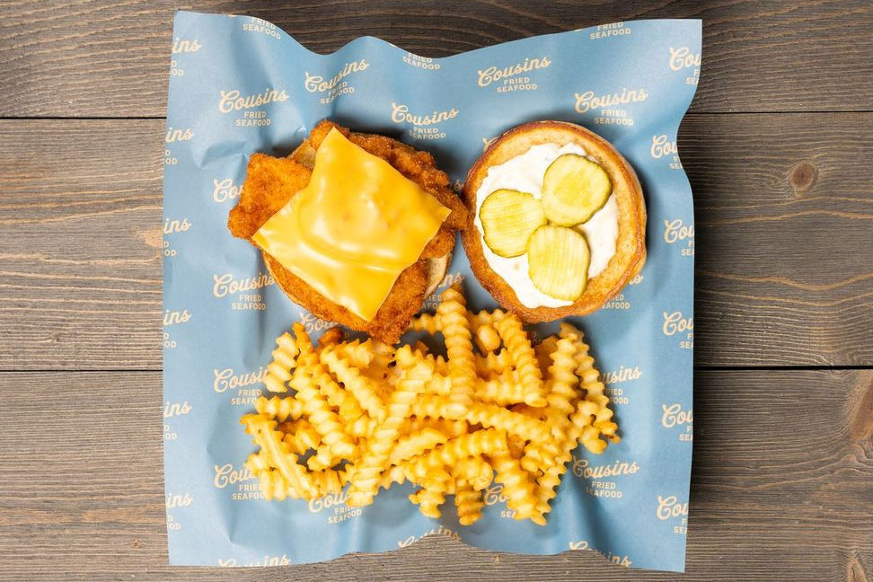 Three items on a blue branded paper: chicken nugget, fries, and a sandwich with pickle slices.
