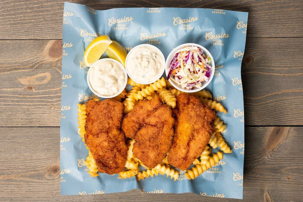 Fried chicken and pasta meal on a blue paper bag with dipping sauces on a wooden surface